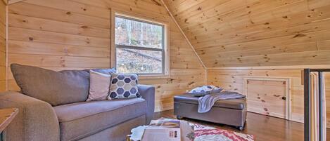 L’intérieur d’un chalet accueillant, avec un plafond en bois, un canapé, une petite table et une fenêtre donnant sur une forêt.