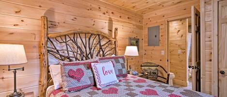 A wooden cabin bedroom with a bed, two nightstands, a lamp, a chair, and a door.
