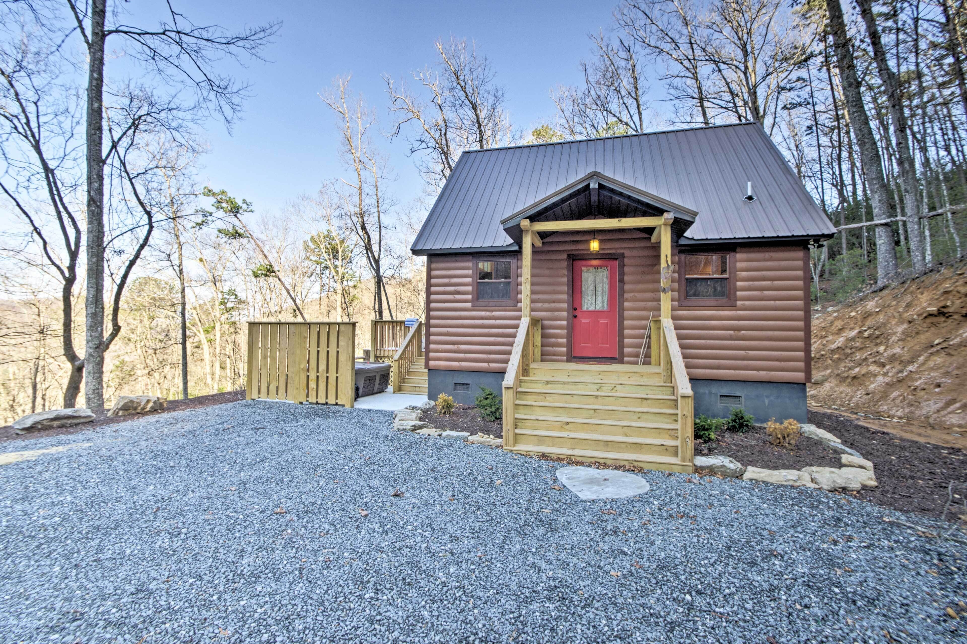 A log cabin with a red door, wooden steps, and a gravel driveway.