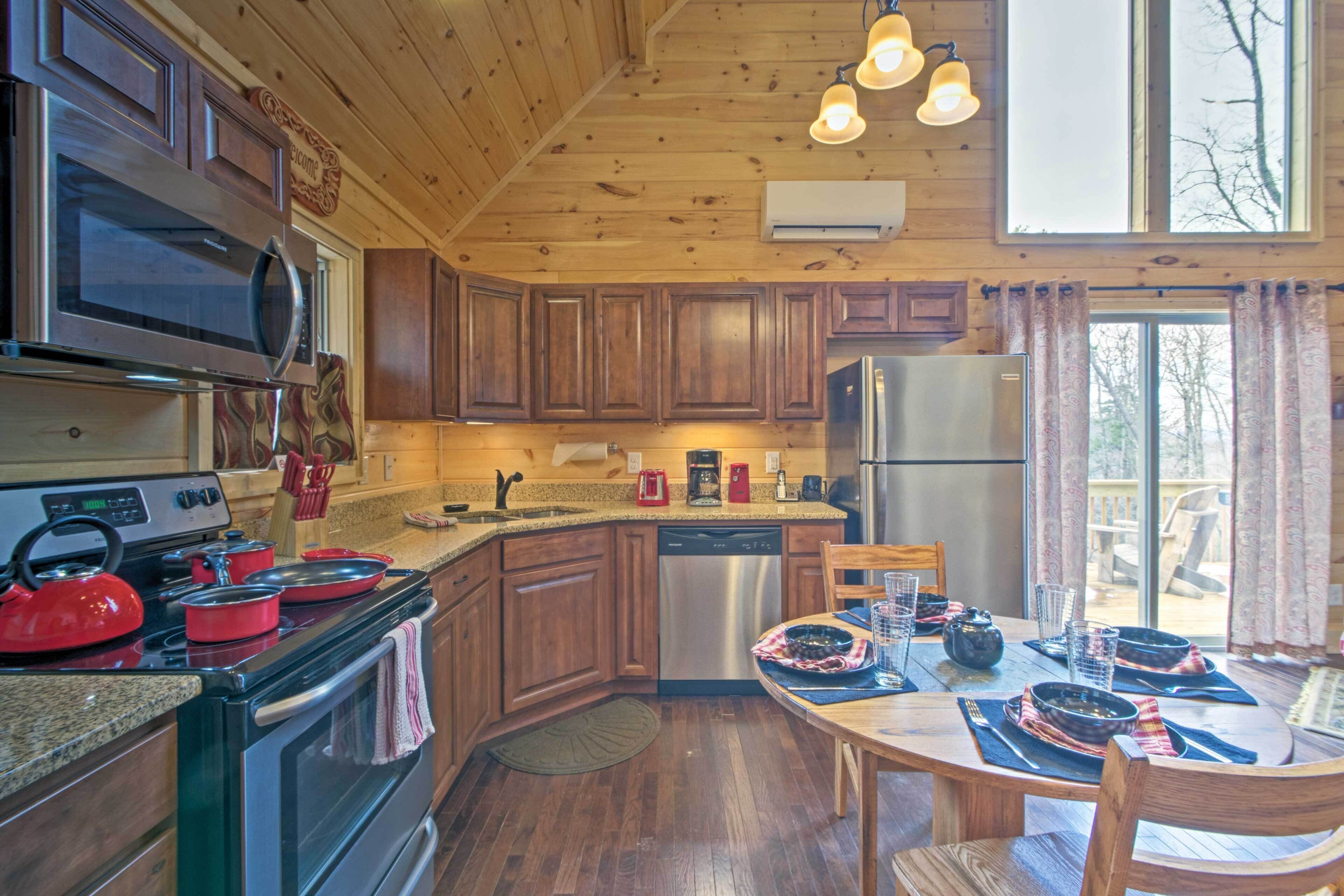 Cucina in legno con un fornello, microonde e frigorifero. C'è un tavolo da pranzo con sedie e una finestra con tende.