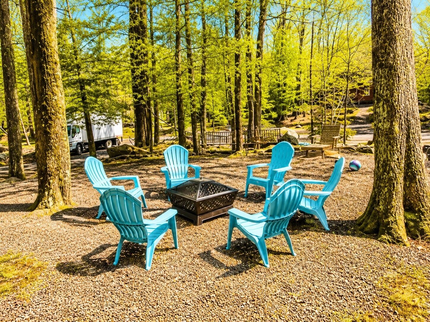 Un terrain de camping avec quatre chaises Adirondack bleues disposées autour d’un foyer noir.