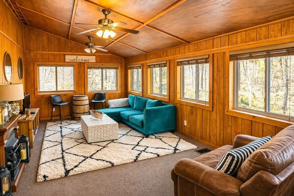 A cozy cabin interior with a wooden interior, a sofa, a loveseat, a coffee table, and a dining area with a bar.