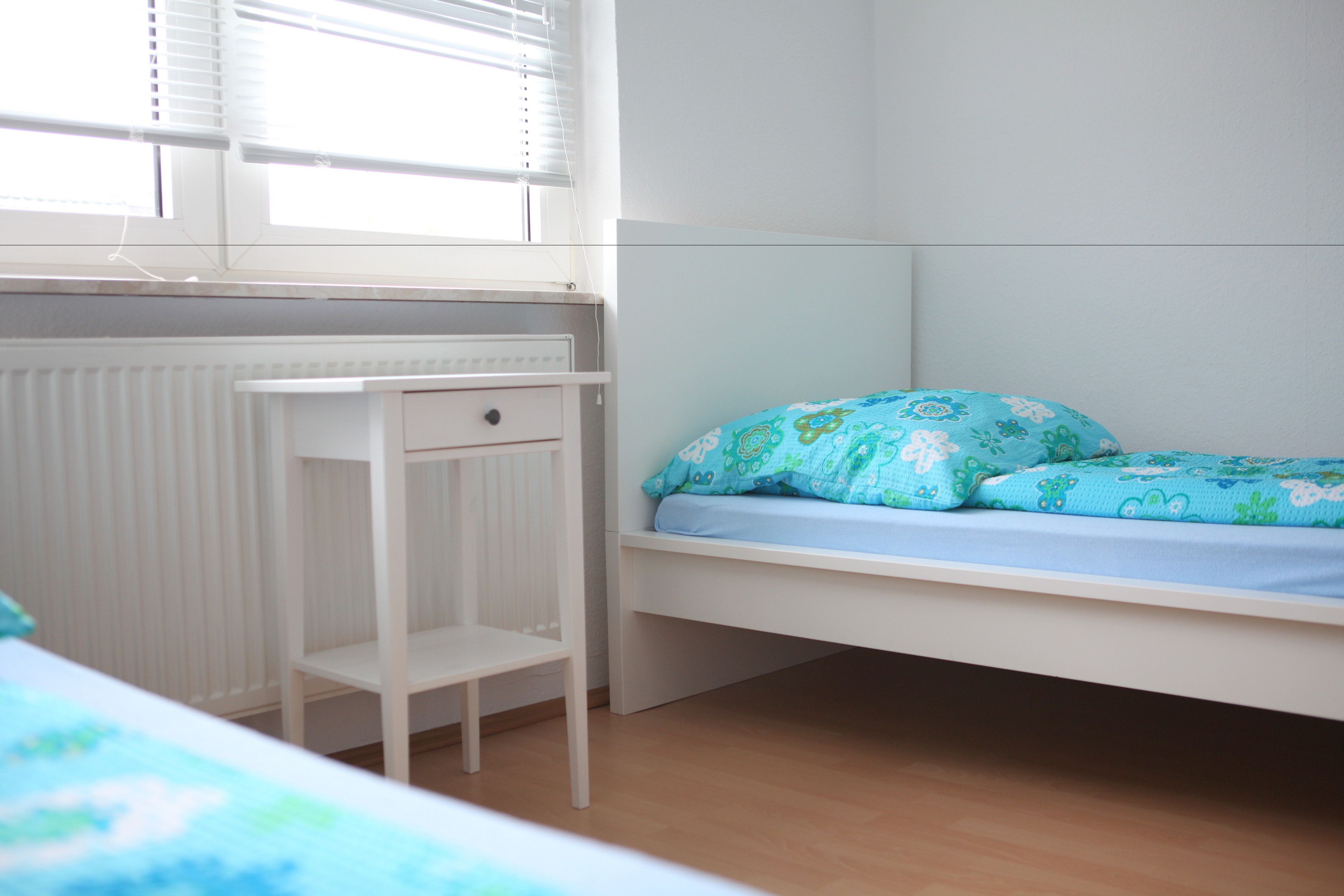 Ein Zimmer mit einem Einzelbett, einem kleinen weißen Schreibtisch und einer Heizung.
