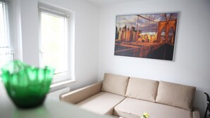Una sala de estar con un sofá color beige, un jarrón verde y un cuadro de un puente.