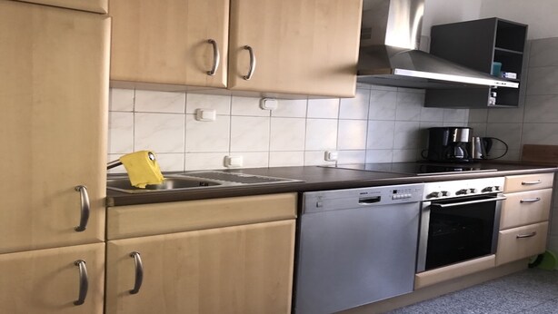 Una cocina con armarios de madera clara, lavavajillas de acero inoxidable, estufa y cafetera.