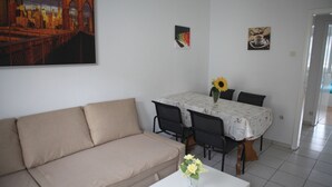 Una sala de estar con un sofá color beige, una mesa de comedor con sillas y un jarrón con flores.