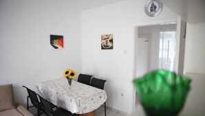 Un comedor con una mesa redonda, sillas y un florero con girasoles. Hay dos cuadros en la pared.