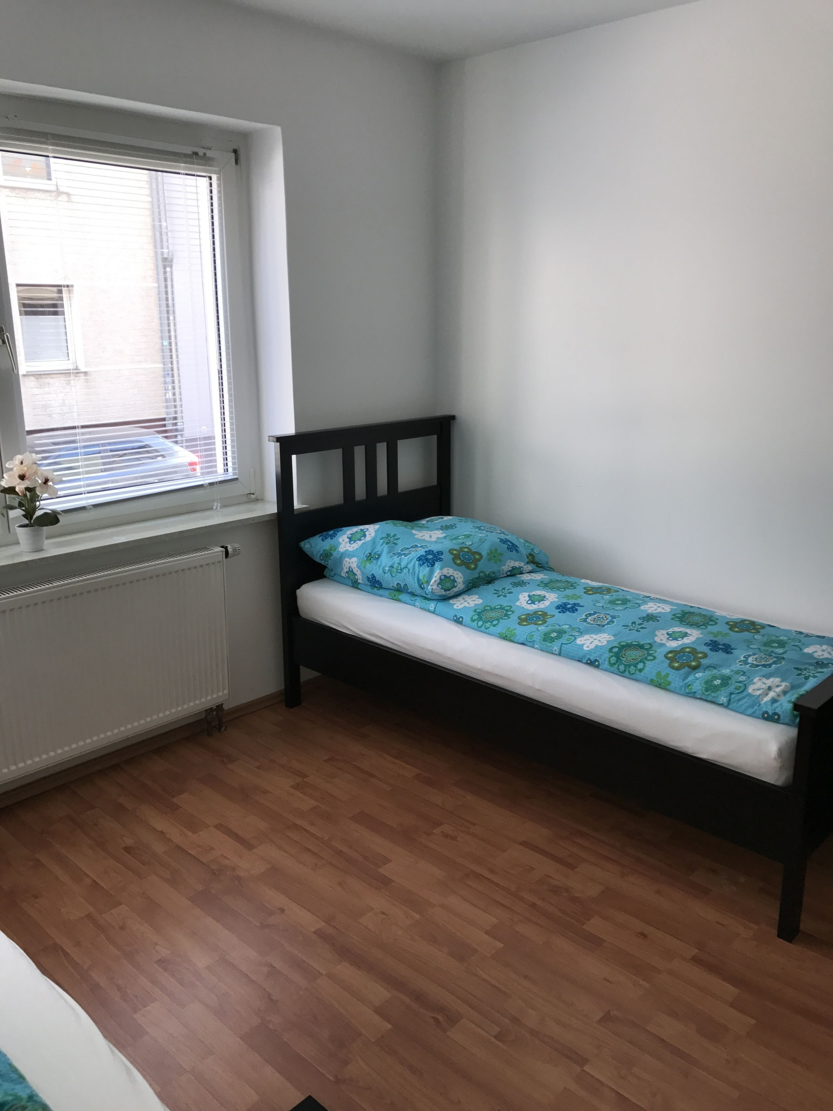 A small room with a single bed, a radiator, and a window with blinds.