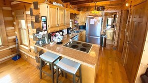 Una cocina de cabaña rústica con armarios de madera, un refrigerador de acero inoxidable, una estufa empotrada y dos taburetes de bar.