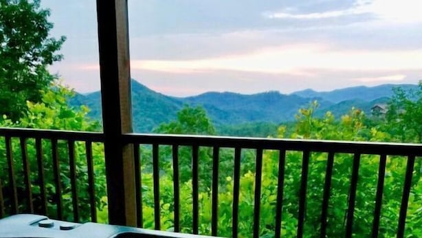 Un jacuzzi en un balcón con vistas a montañas y follaje.