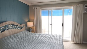 A hotel room with a bed, a nightstand, a lamp, and a view through a sliding glass door. - 13 on the beach 10, Ocean City, MD, USA - Beautiful direct ocean front 3 bedroom 2 bath townhome (Ocean City)