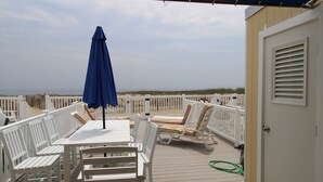 A deck with white furniture, a blue umbrella, and a view of the beach. - 13 on the beach 10, Ocean City, MD, USA - Beautiful direct ocean front 3 bedroom 2 bath townhome (Ocean City)