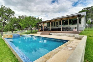 Ein Schwimmbad mit überdachter Terrasse, einer kleinen Sitzgelegenheit im Freien und einem umzäunten Garten.