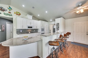 A kitchen with white cabinets, a granite countertop, and a bar area with stools.