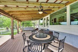 A covered outdoor patio with a round table and chairs, wooden beams, and a ceiling fan.