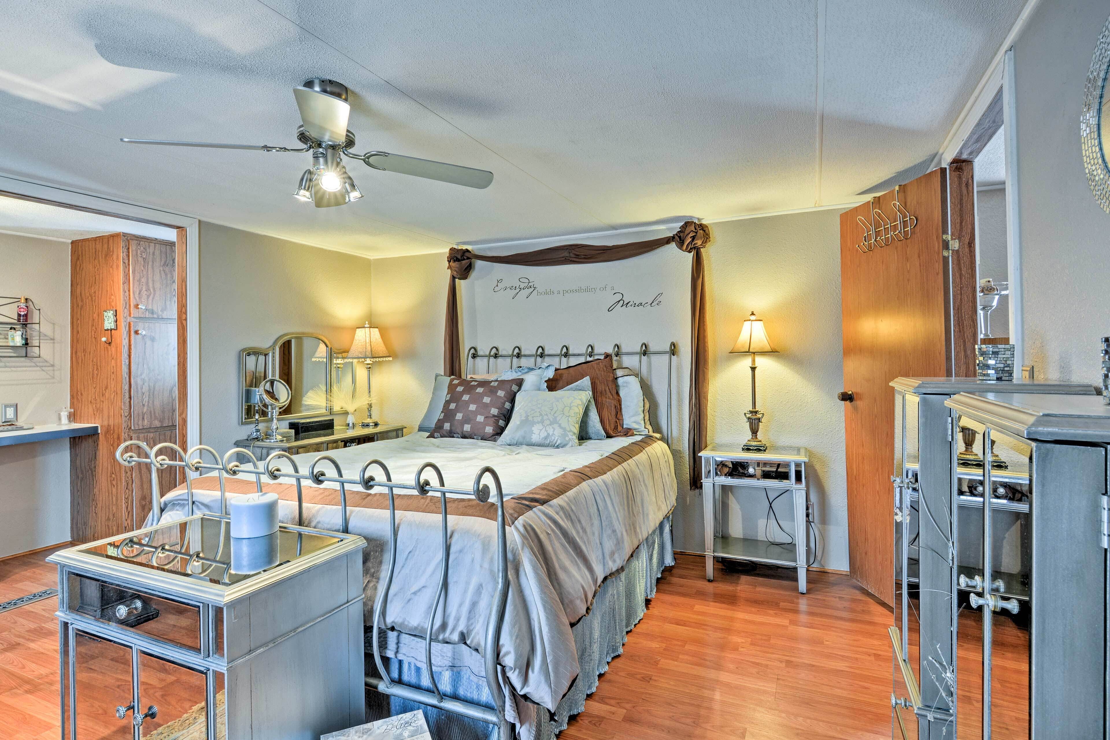 A bedroom with a four-poster bed, bedside tables with lamps, a ceiling fan, and a wall with a motivational quote.