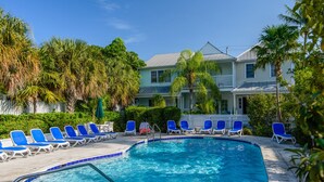 A swimming pool with blue chairs, surrounded by palm trees and a two-story building with a white fence. - Amberjack at The Truman Annex in Key West (Key West)