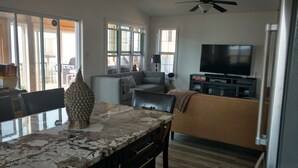 A modern living room with a large TV, a dining area with a marble table, and a sofa.