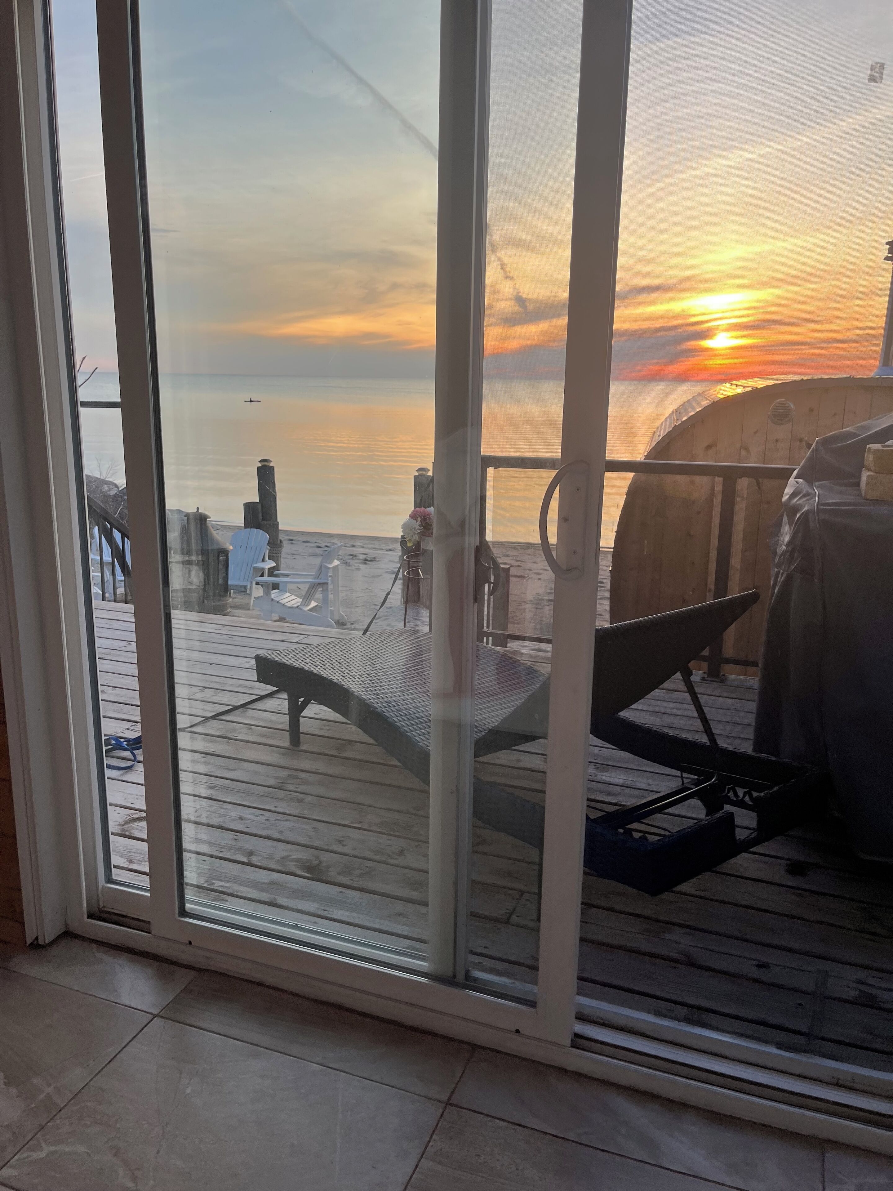 A view from a room with a large glass door overlooking a wooden deck with a grill and outdoor furniture.