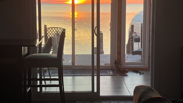A room with a sliding glass door leading to a balcony with a view of the sunset over the water.