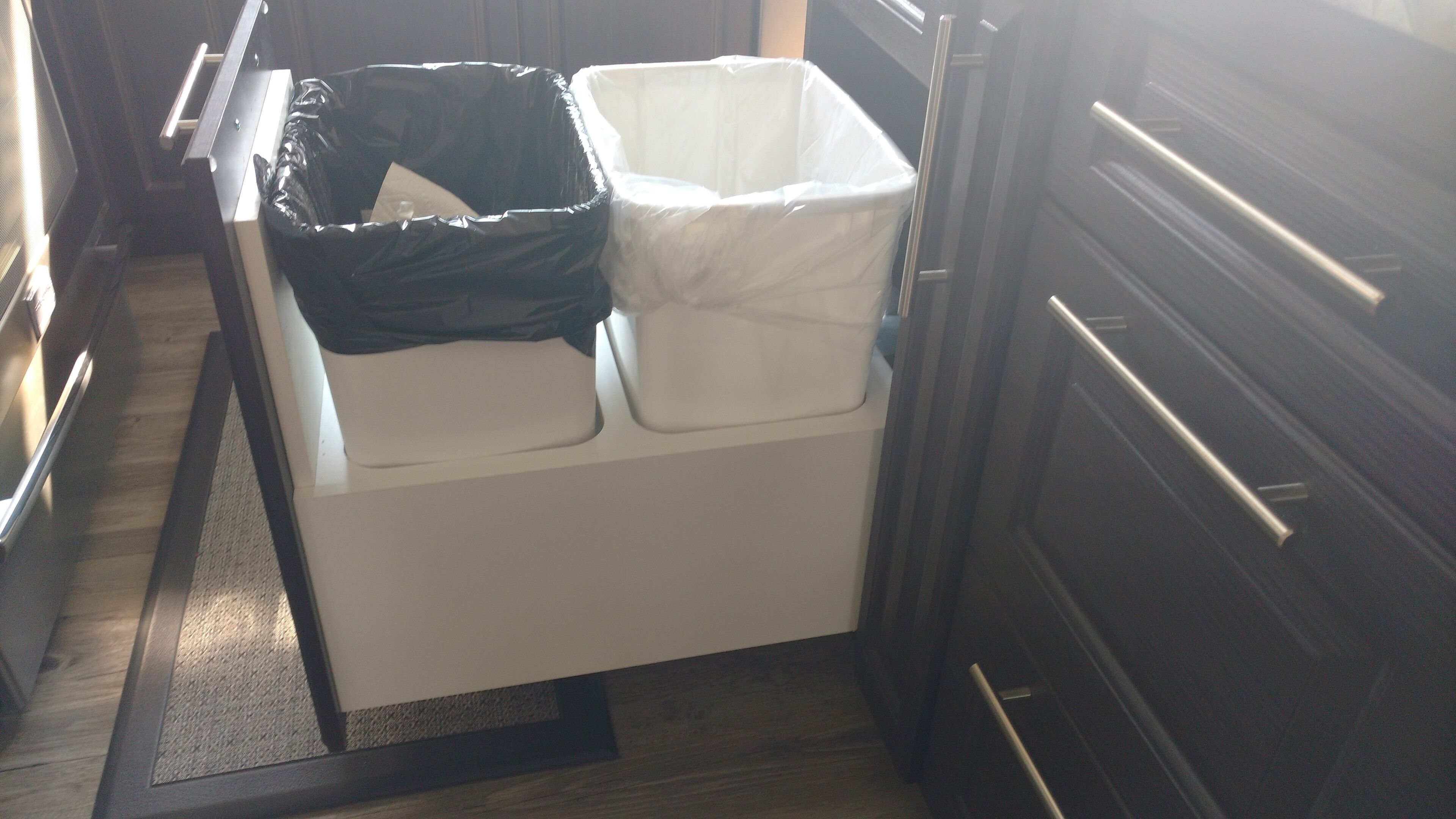 A kitchen with a white countertop, a black trash bin, and a white trash bin.