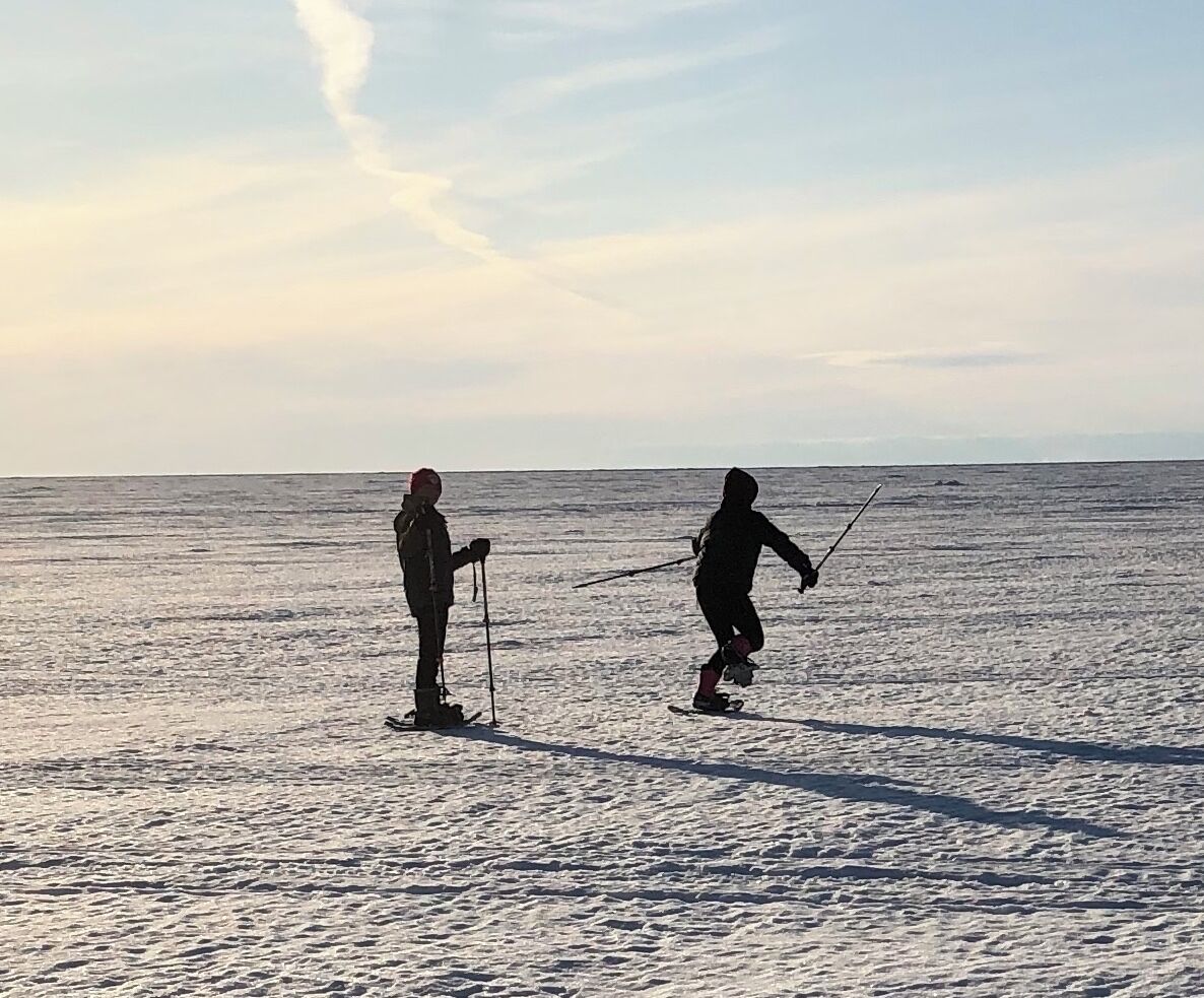 Two people skiing on a snowy surface with a clear sky in the background.