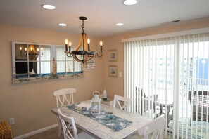 A dining area with a table, chairs, a chandelier, a window with a view, and a balcony with white railings.
