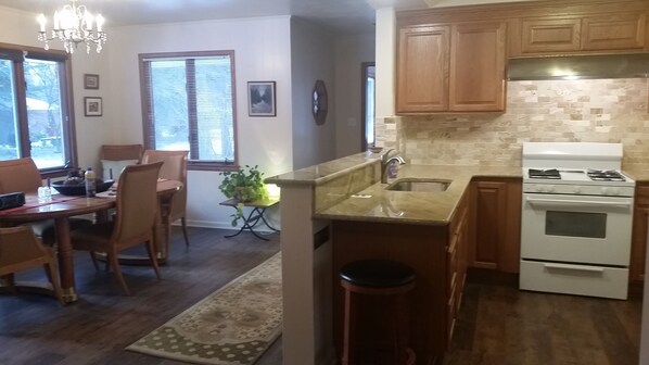 A kitchen with wooden cabinets, a stove, and a sink. There is a dining area with chairs and a table. - A sanctuary just 15 minutes from Detroit (Southfield)