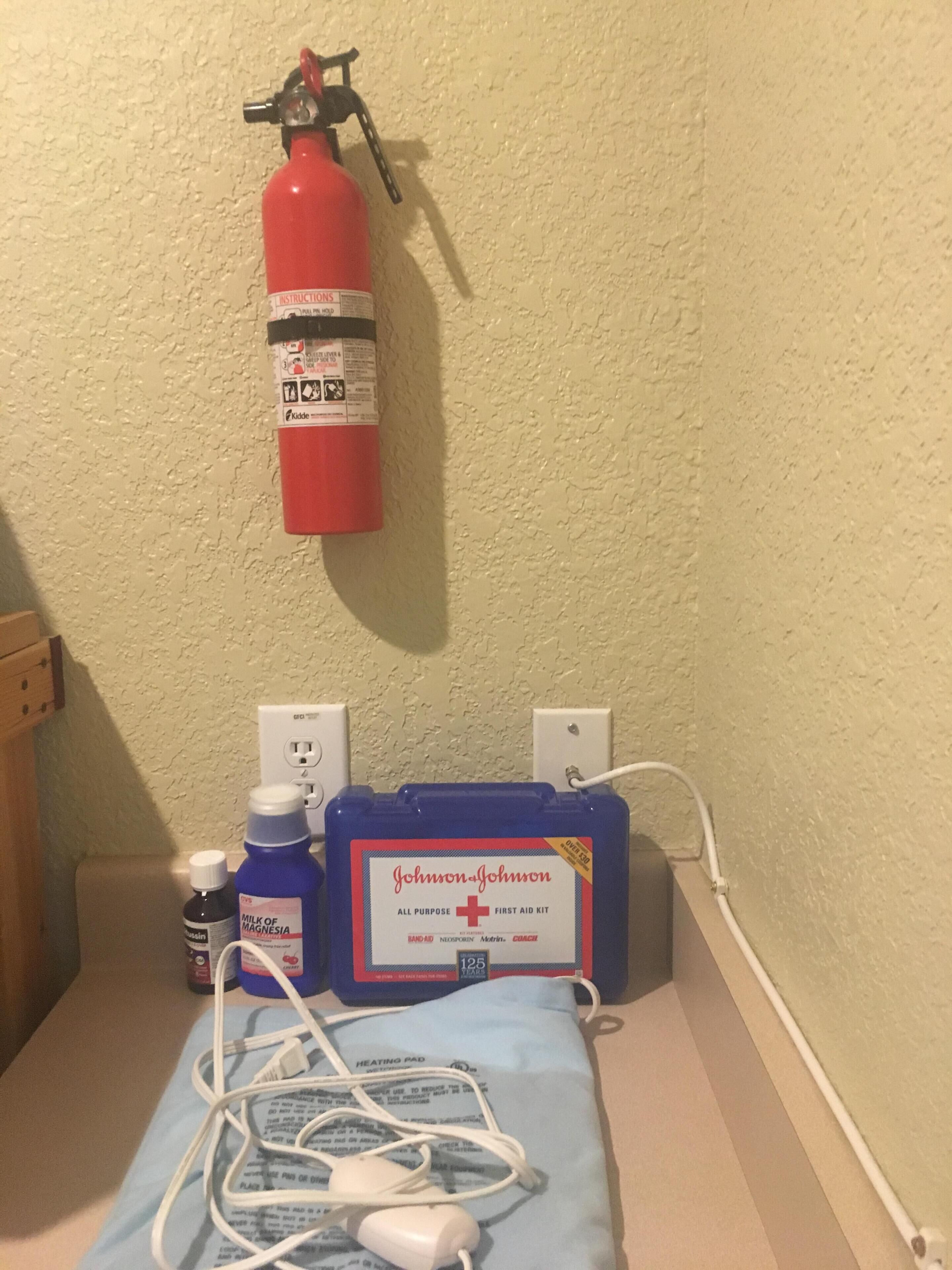 Um kit médico, um extintor de incêndio e uma caixa azul de primeiros socorros sobre uma mesa de cabeceira.