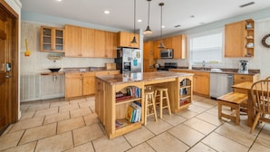 A kitchen with wooden cabinets, a central island with stools, a microwave, and a refrigerator. - Large 6 Bdrm home with amazing Gulf Views, Easy Beach Access, and Private Pool (Gulf Shores)
