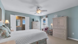 A bedroom with a bed, a ceiling fan, a dresser, a chair, and a lamp.