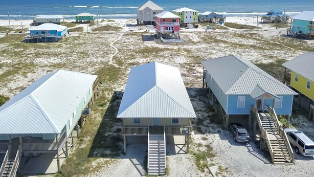 A coastal area with several beach houses on stilts, connected by wooden walkways, and a clear view of the ocean.