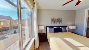 Habitación de hotel con un ventanal grande, cama con ropa blanca, dos lámparas de noche y un adorno en la pared.