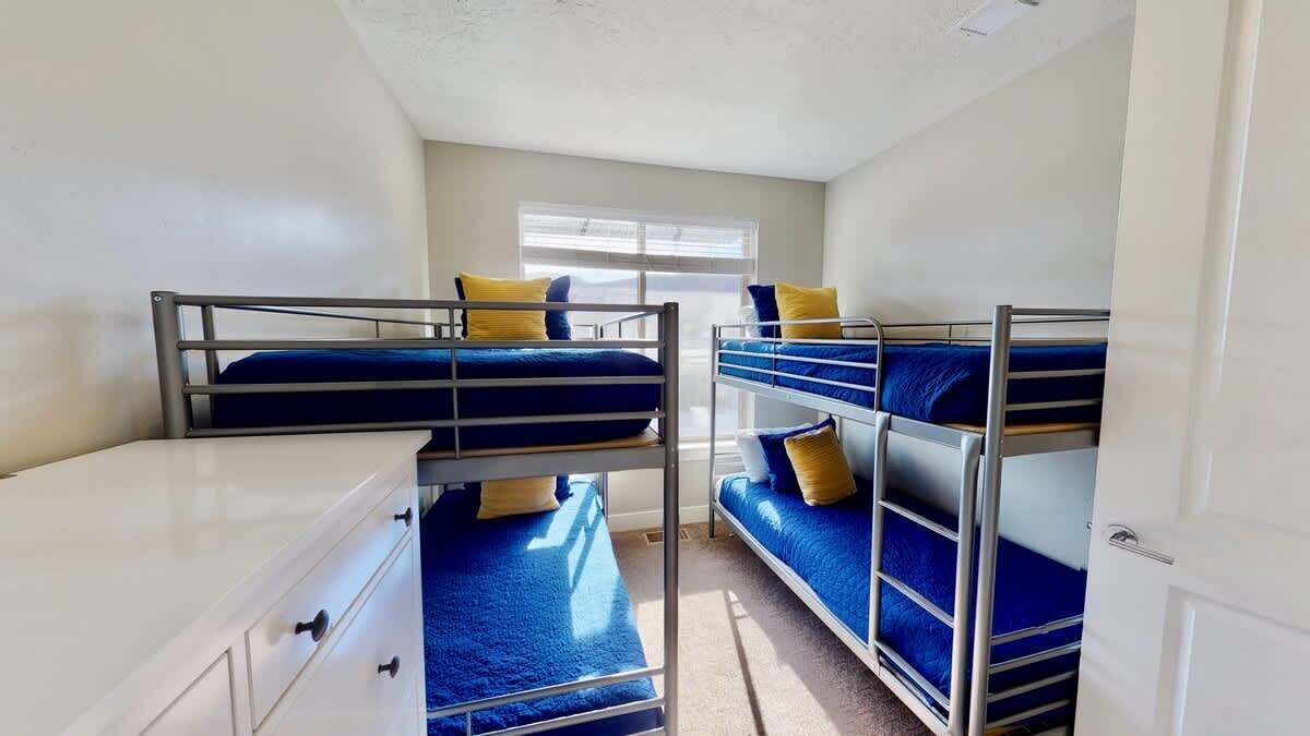 A dormitory room with bunk beds, a desk, and a window.