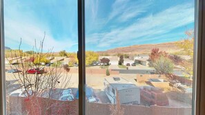 A view through a window of a parking lot with RVs and cars, a building with a flat roof, and a hilly landscape in the background.