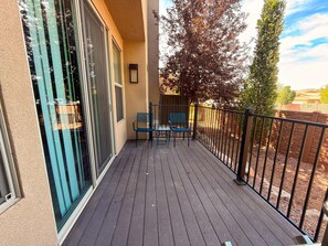 A balcony with a wooden deck, two chairs, and a table.