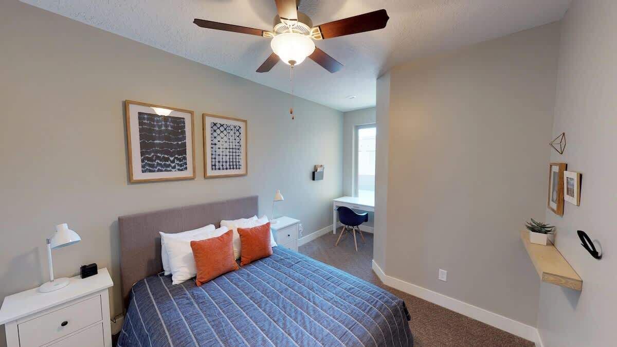 Ein Schlafzimmer mit einem Bett, einem Schreibtisch, einem Stuhl und einem Deckenventilator.