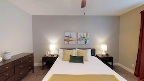 Un dormitorio con una cama grande, dos lámparas de noche, un aparador y dos cuadros abstractos en la pared.