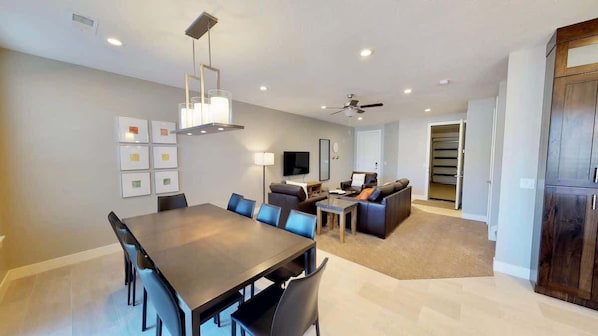 Una sala de estar moderna con comedor, un conjunto de sofás, un televisor y un ventilador de techo.