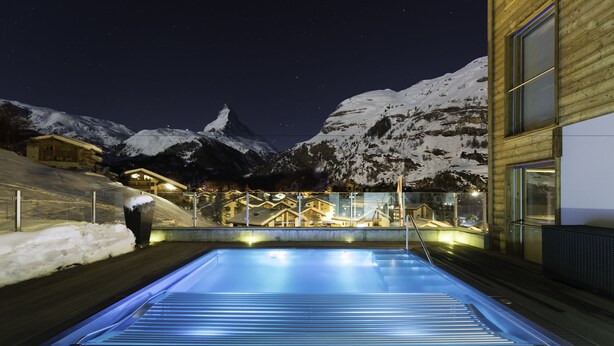 A swimming pool with a view of snow-covered mountains at night. - Chalet Nepomuk (Zermatt)