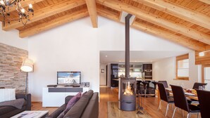A modern living room with a fireplace, a sofa, a television, and a dining area with chairs and a table. - Chalet Nepomuk (Zermatt)