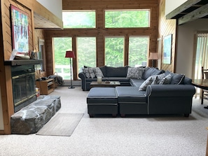 A cozy living room with a fireplace, large windows, a sectional sofa, and a stone accent wall.