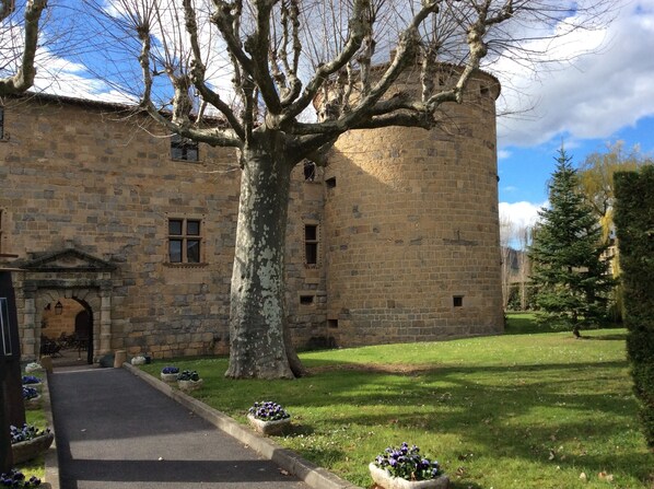 A stone building with a large tree in front, a paved path, and a grassy area with flower beds. - Stone Cottage With Private Sun Terrace And Mountain Views (Sougraigne)