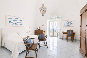 A bedroom with a bed, two chairs, a dresser, and a chandelier.