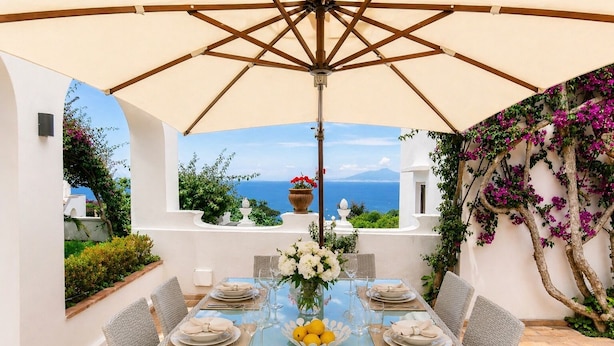 Ein Tisch für sechs Personen mit Meerblick, einer Pergola und einer weißen Wand.
