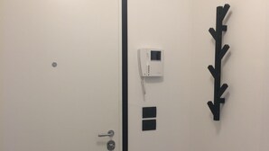 Puerta blanca con marco negro, un portero automático instalado en la pared y una obra de arte negra.