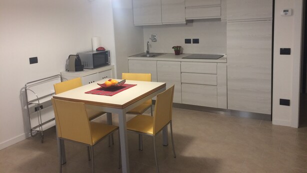 Cocina compacta con armarios blancos, microondas, fregadero y comedor con mesa y sillas.