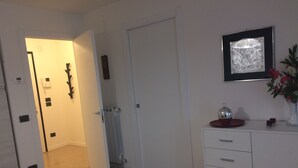 Habitación de hotel con un armario blanco, un radiador, una obra de arte enmarcada y un jarrón con flores.
