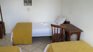 A small, simple room with a single bed, a wooden chair, and a small table. - La Villa Hotel (Cordeirópolis)