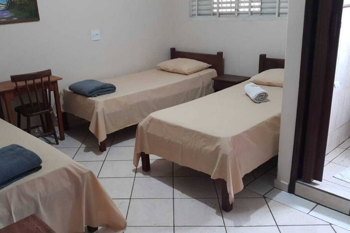 Une chambre avec trois lits simples, une chaise en bois et une petite table.